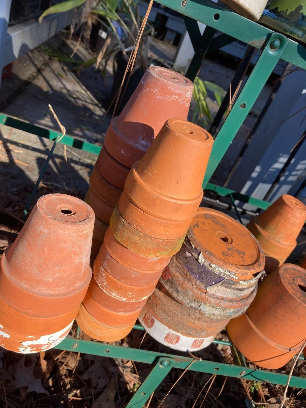 A green metal rack holding stacked empty orange clay flower pots outdoors on a sunny day.