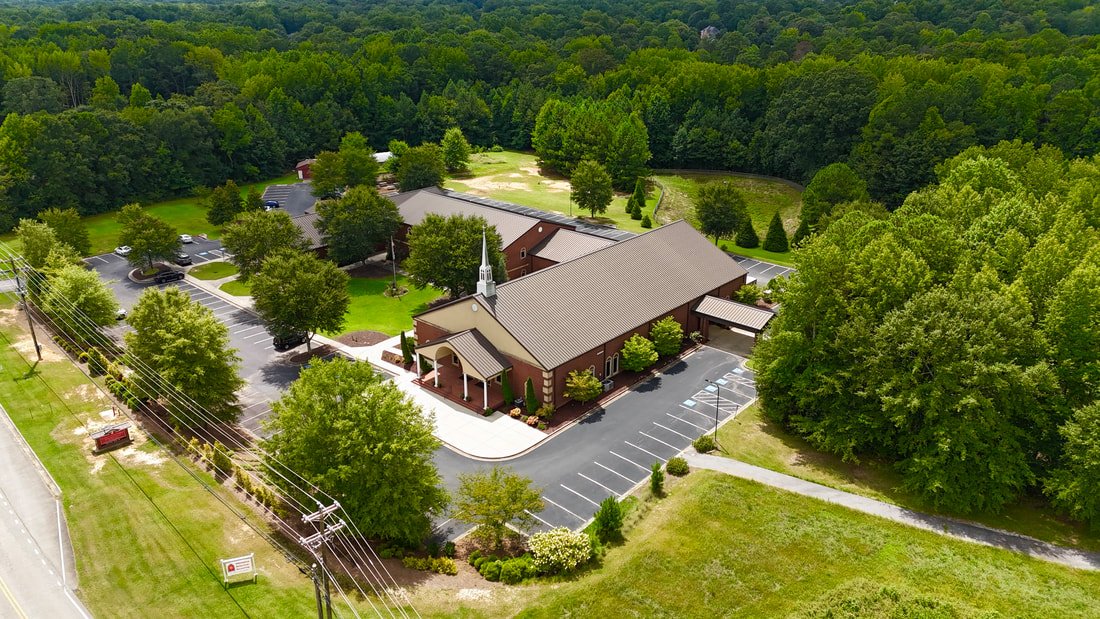 A church with a parking lot surrounded by trees in a rural area.