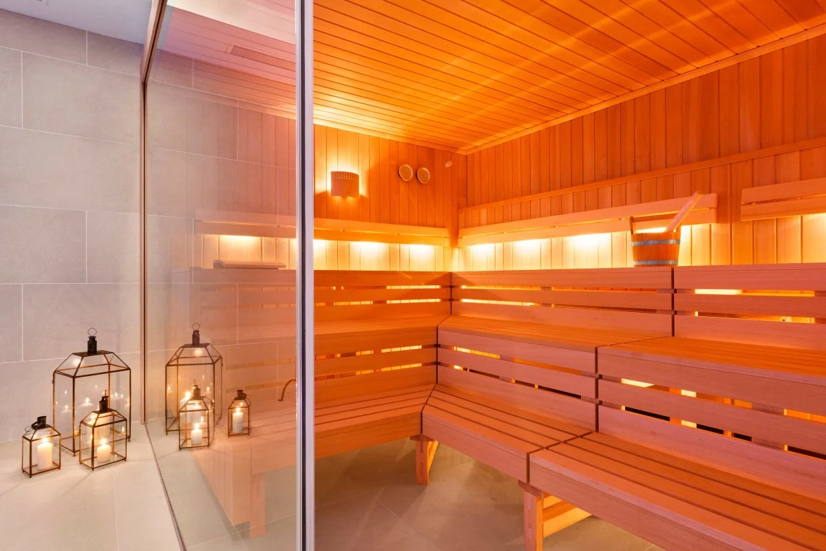 Interior of a sauna with wooden benches, a bucket with a ladle, and glass lanterns with candles inside.