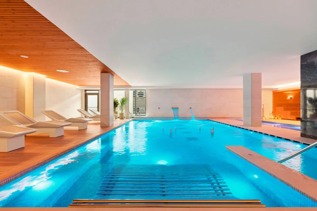 Indoor pool area with lounge chairs, potted plants, and bright lighting.