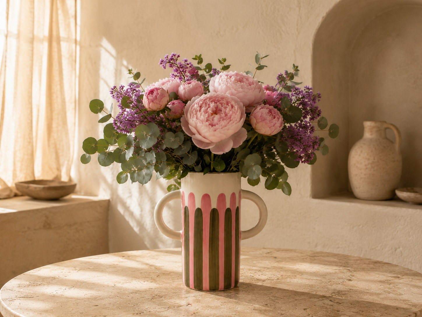 Un bouquet de fleurs roses et violettes dans un vase à rayures rose, blanc et vert, posé sur une table en marbre.