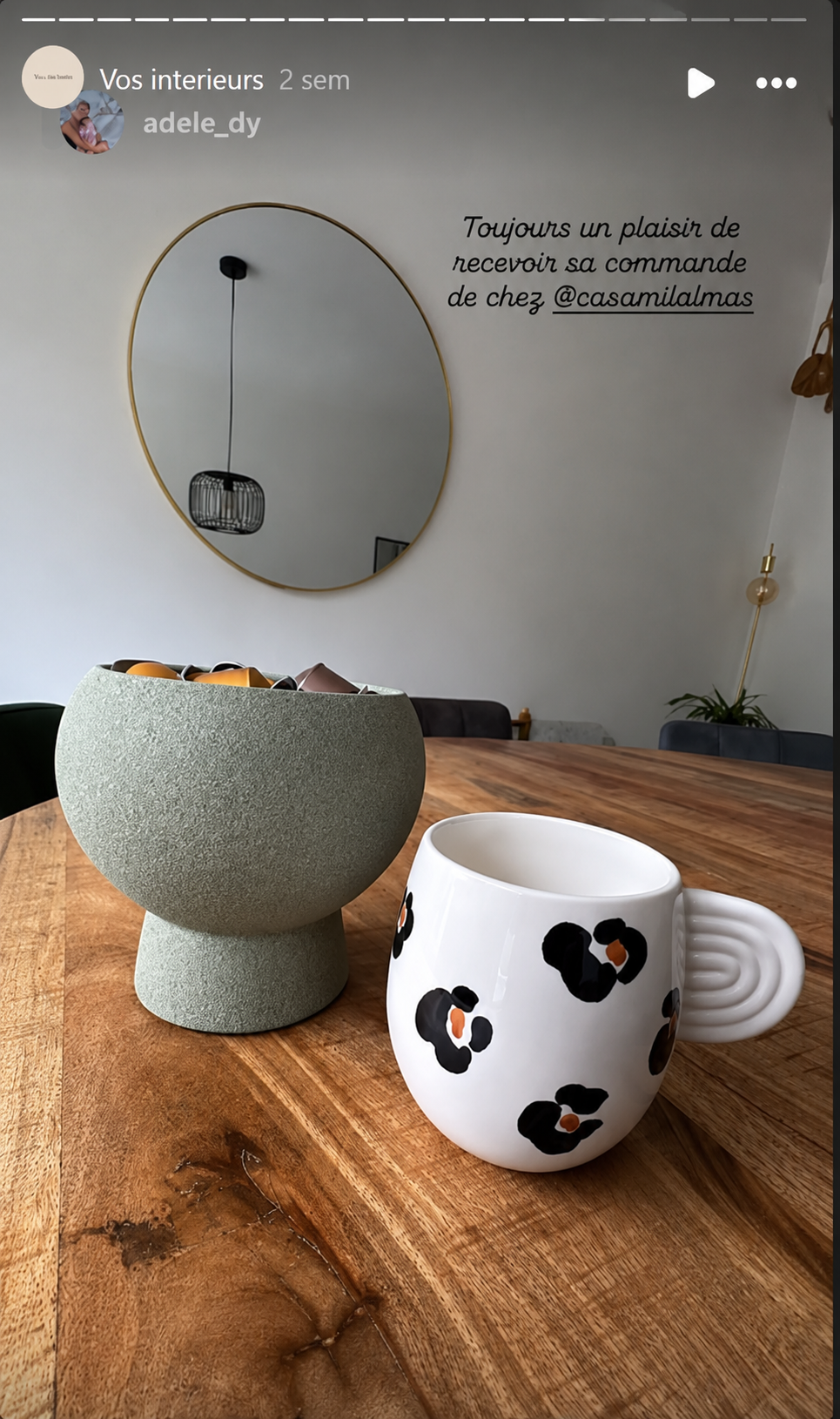 Un mugs aux motifs léopard et un vase en céramique vert, posés sur une table en bois massif. En arrière-plan, un miroir rond au cadre doré, et un mur blanc avec texte écrit en français.