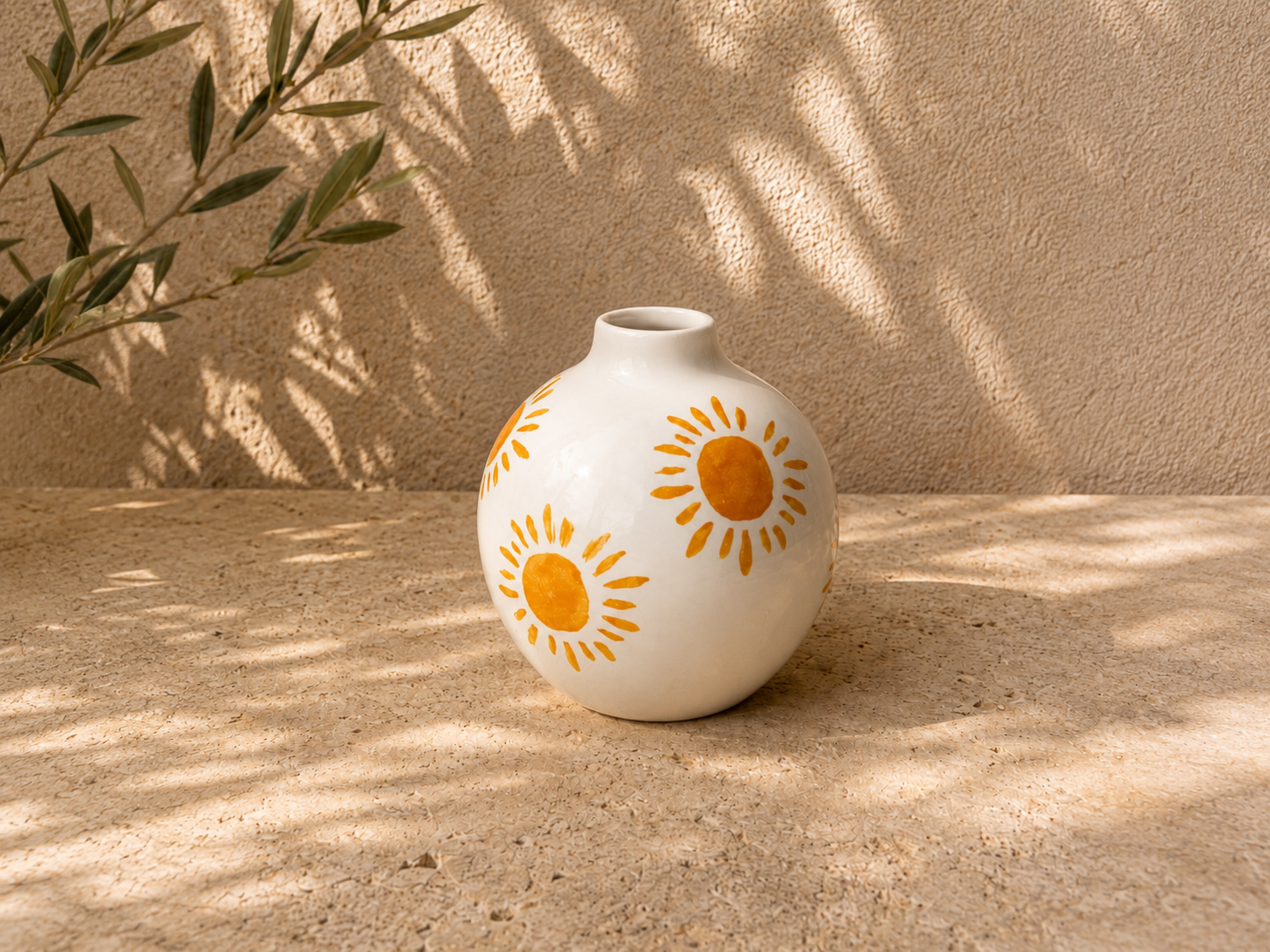 Vase blanc avec motifs de soleils oranges sur une surface en pierre, ambiance ensoleillée avec ombres de feuillage
