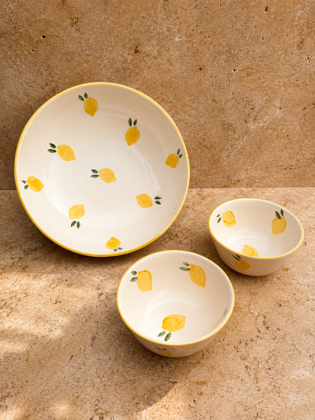 Ensemble de duex bols et d'un saladier, décorés de motifs de citrons jaunes avec des feuilles vertes, placés sur une surface de pierre naturelle.