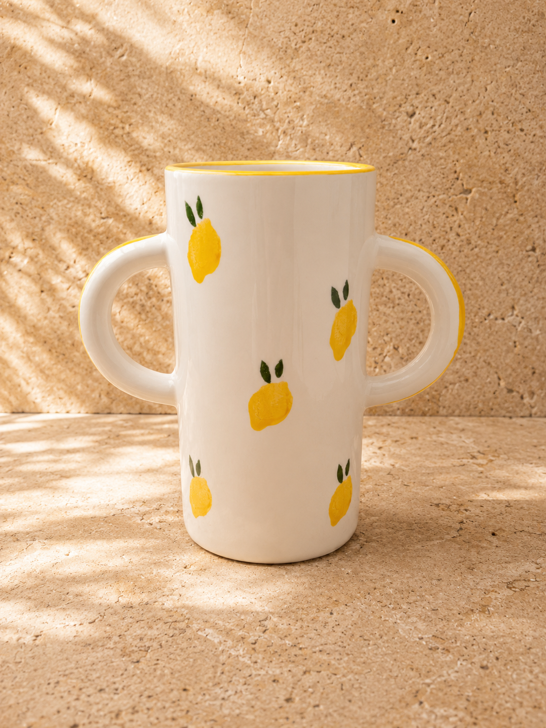 grand Vase blanc décoré de citrons et de feuilles, placé sur une surface de pierre, avec des ombres de rayures lumineuses.