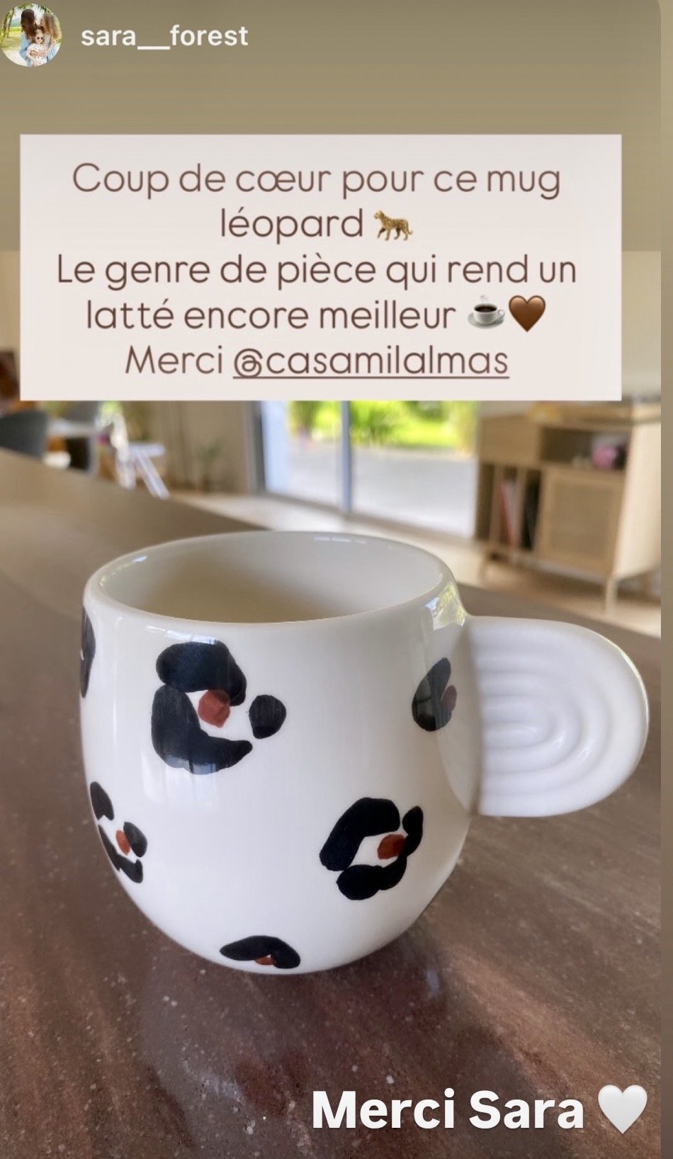 Un mug avec un motif léopard noir et roux, placé sur une table en bois, avec une pièce moderne et lumineuse en arrière-plan.