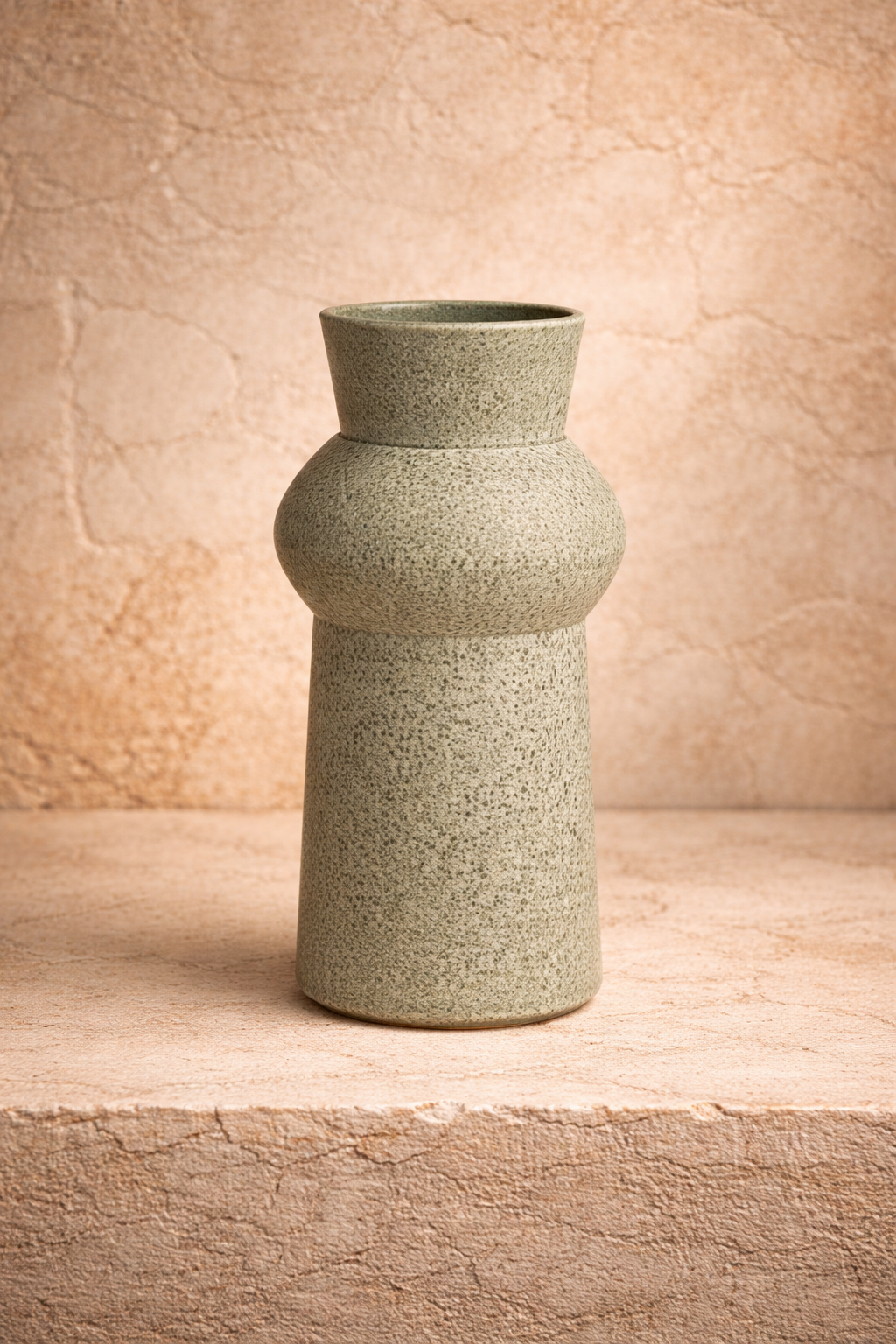 Vase en céramique artisanal portugais en vert sauge aspect mat avec une surface texturée sur un socle en pierre contre un mur beige