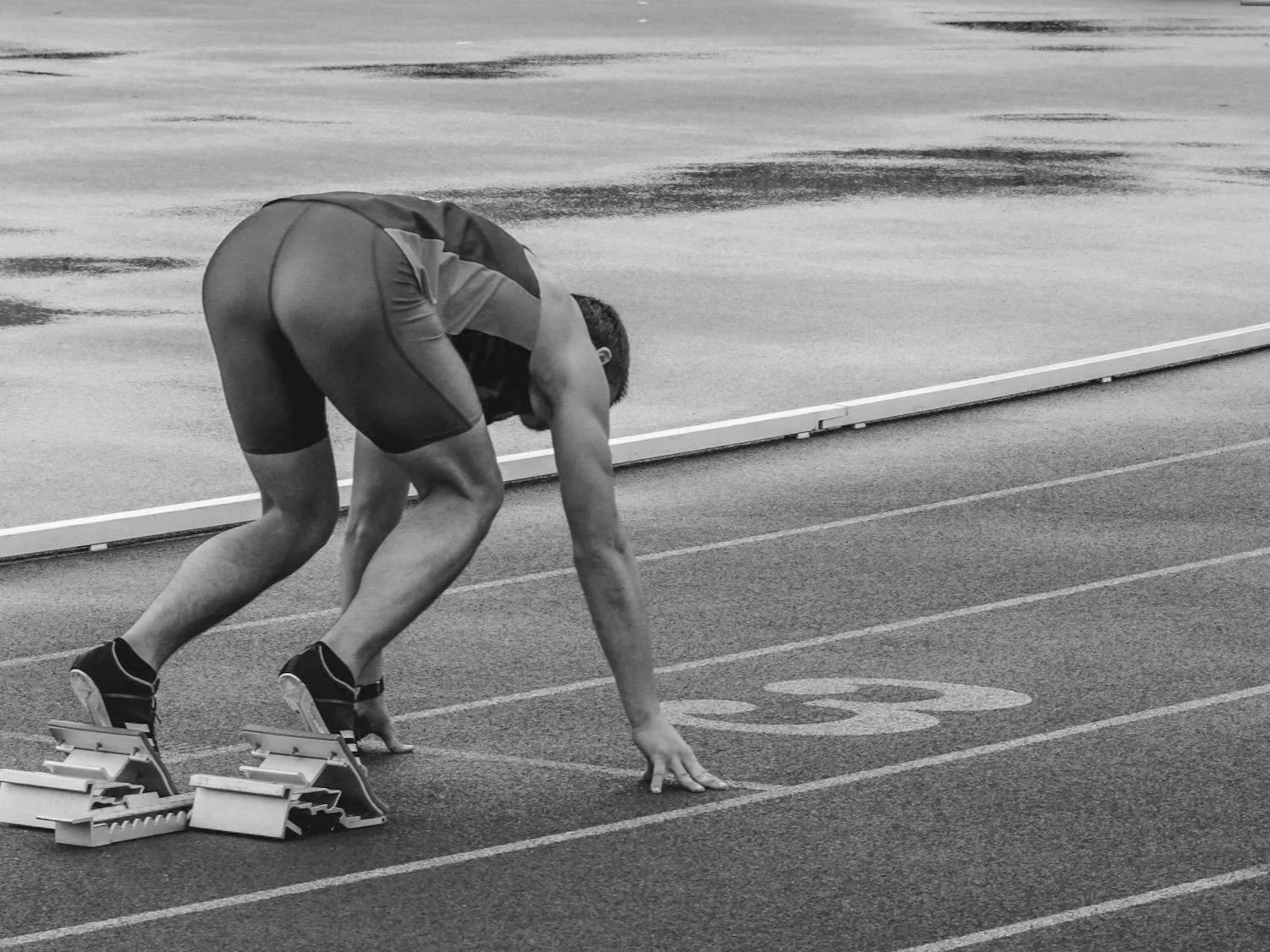 A male sprinter in starting position on a track, ready for a race, with starting blocks behind him.