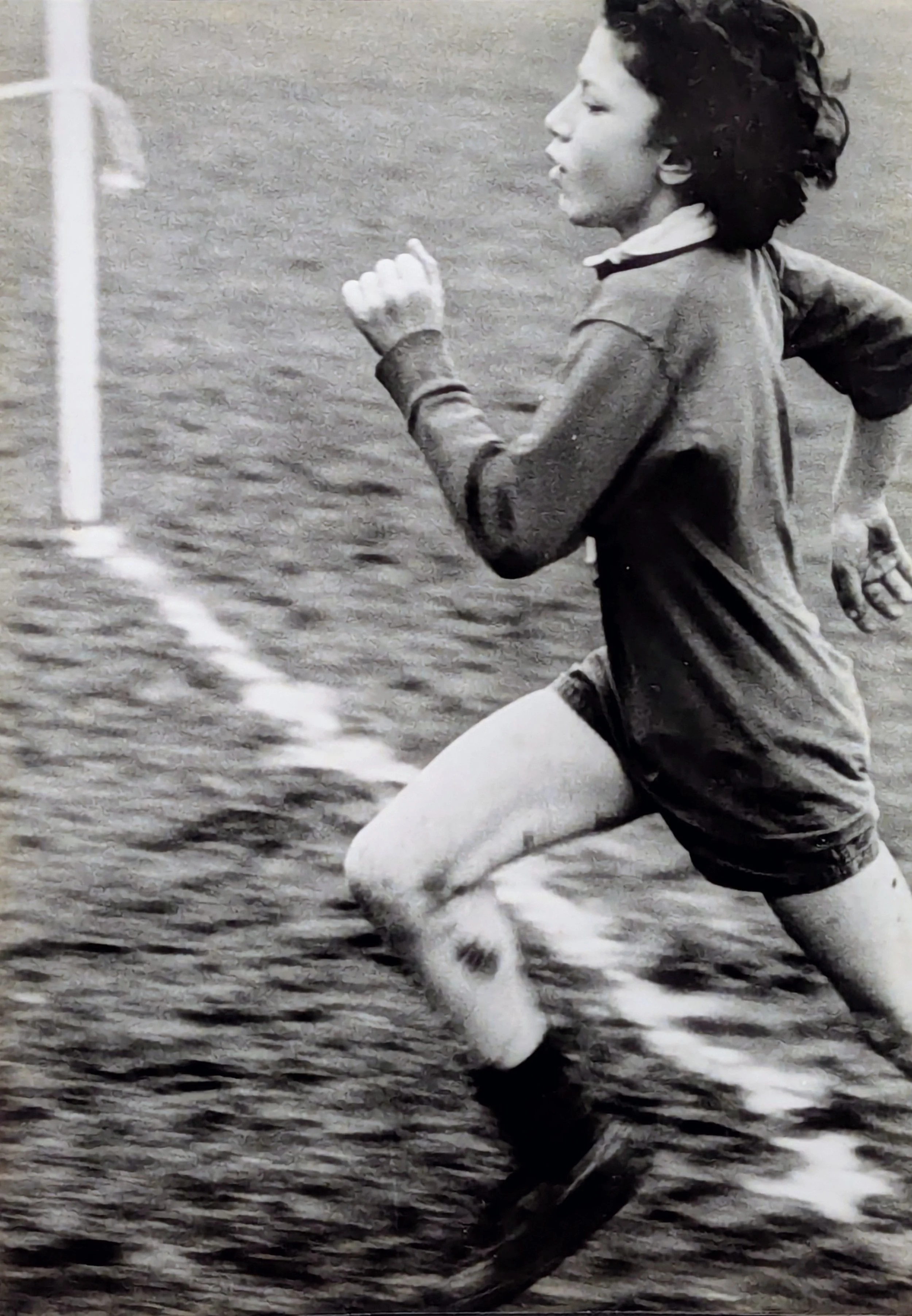 A young girl running outdoors, wearing athletic clothing, on a grassy field.