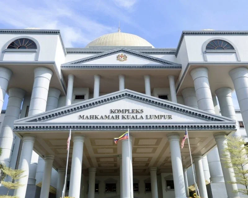 The Kuala Lumpur Court Complex building with white columns and a large gold dome, featuring Malaysian and American flags at the entrance.