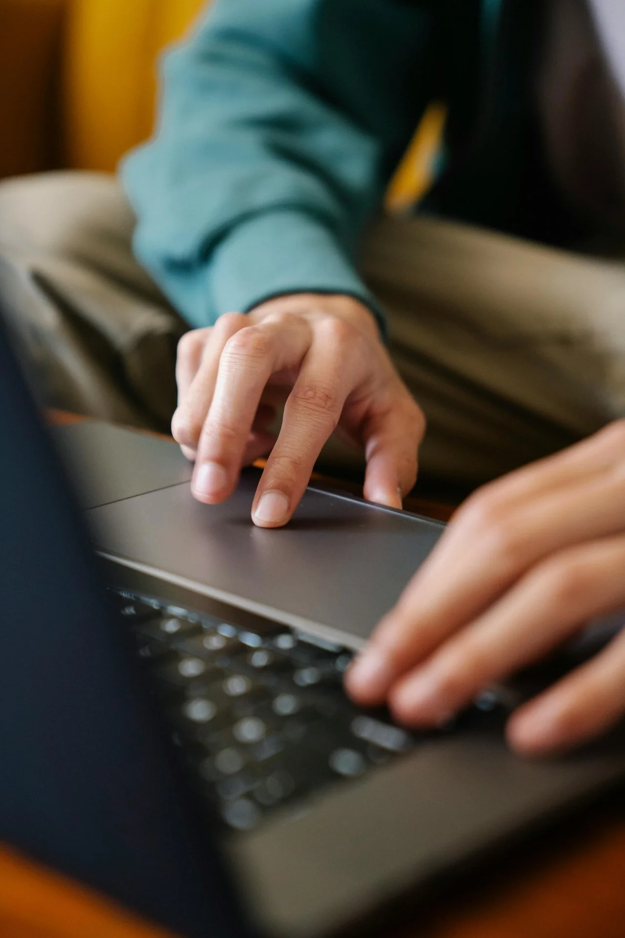 A person using a laptop, with their left hand on the keyboard and their right hand touching the touchpad.