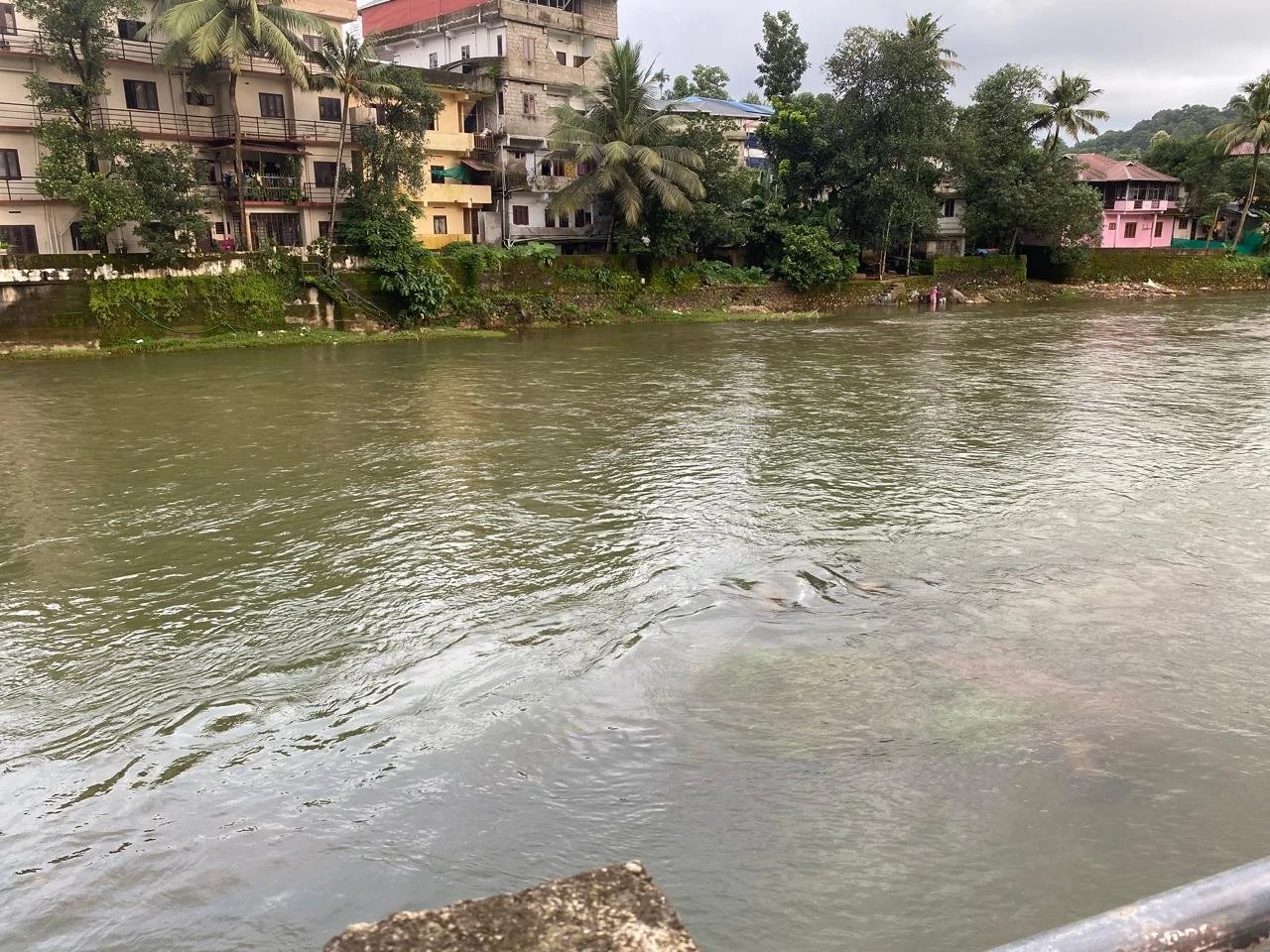 River with muddy water in a residential area with multi-story buildings, trees, and boats.