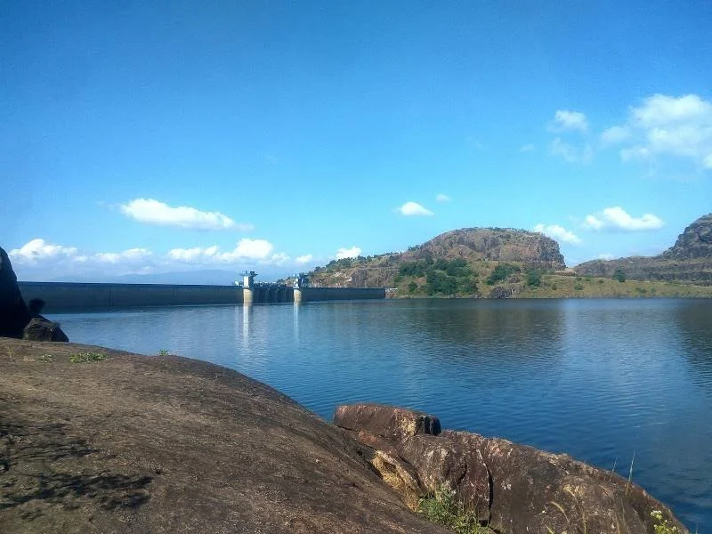 A large body of water with a dam and hills in the background under a blue sky with clouds.