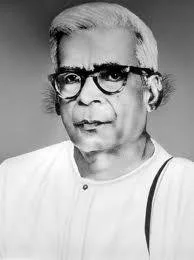 Black and white photo of an older man with glasses and white hair, wearing a white shirt.