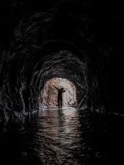 Silhouette of a person standing at the entrance of a dark tunnel with water inside, light shining from beyond the tunnel opening.