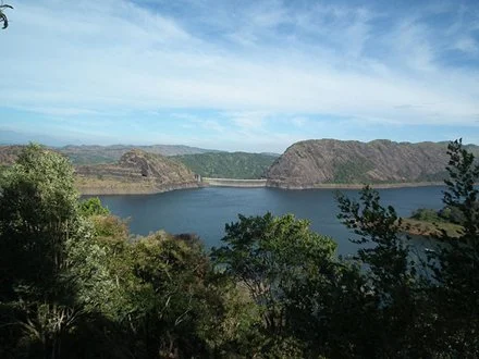 A scenic view of a lake surrounded by hills and trees, with a partly cloudy sky overhead.