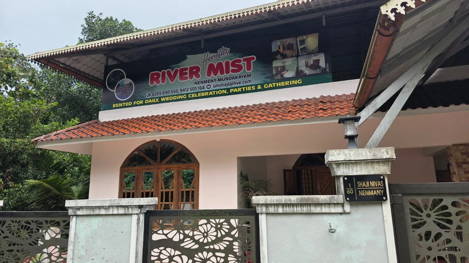 A two-story house with a signboard for River Mist, a rental for weddings, parties, and gatherings. The house has a tiled roof, large arched windows, and a gated front with lush greenery surrounding it.