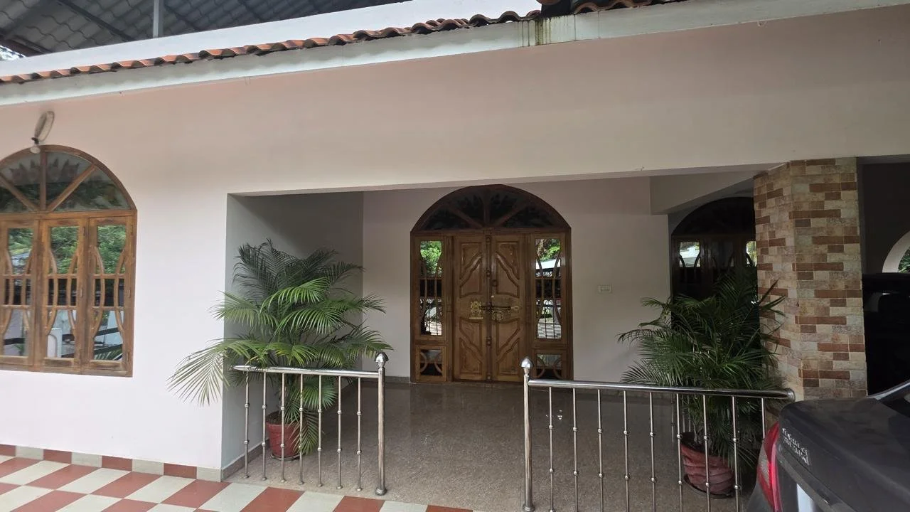 House entrance with wooden double doors, potted plants on either side, and a metal railing in front.
