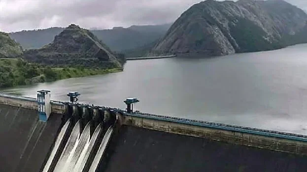 A dam with water flowing through turbines, surrounded by green hills under cloudy skies.