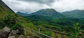 Hilly green landscape with a dirt path and wooden fence under a cloudy sky.