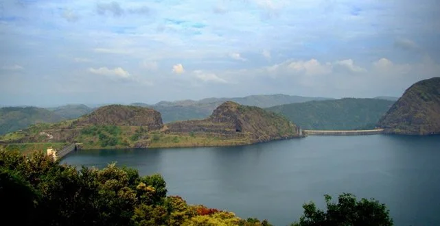 A large body of water surrounded by hills and mountains with partly cloudy sky.