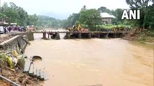 Bridge over a muddy river with onlookers and construction equipment in the background.
