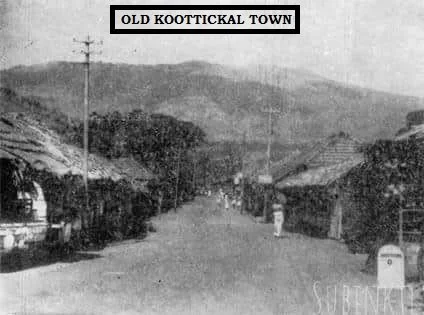 Historical black and white photo of a town street labeled Old Koottickal Town, showing buildings, utility poles, and a mountain backdrop.
