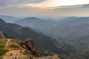 Mountain landscape with rolling hills and valleys, a dirt trail, and a few people hiking.
