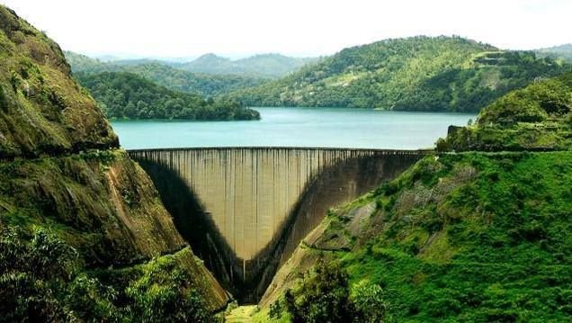 Dam in a lush green valley with a reservoir behind it, surrounded by forested hills.