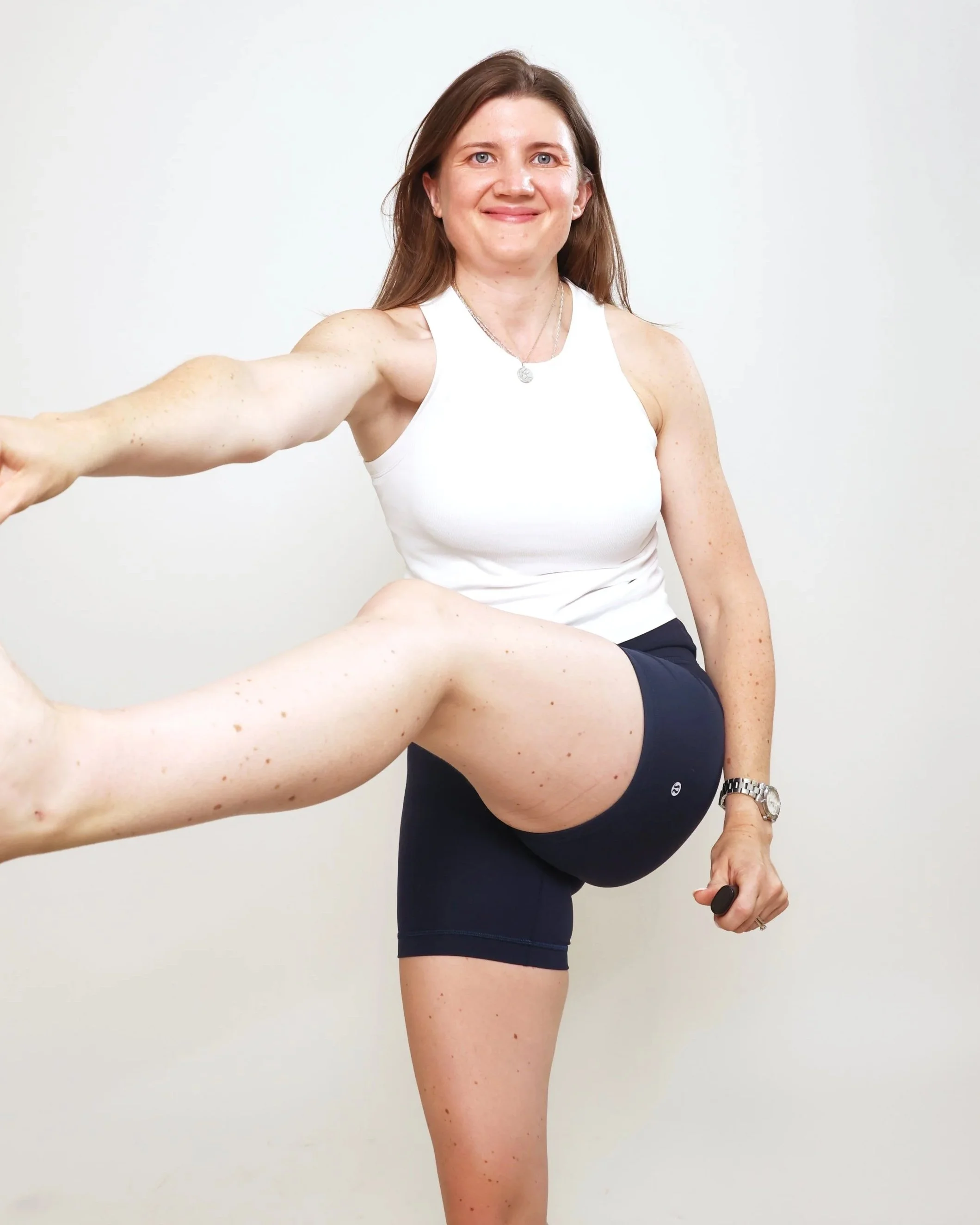Woman in athletic wear stretching her leg against a plain white background.