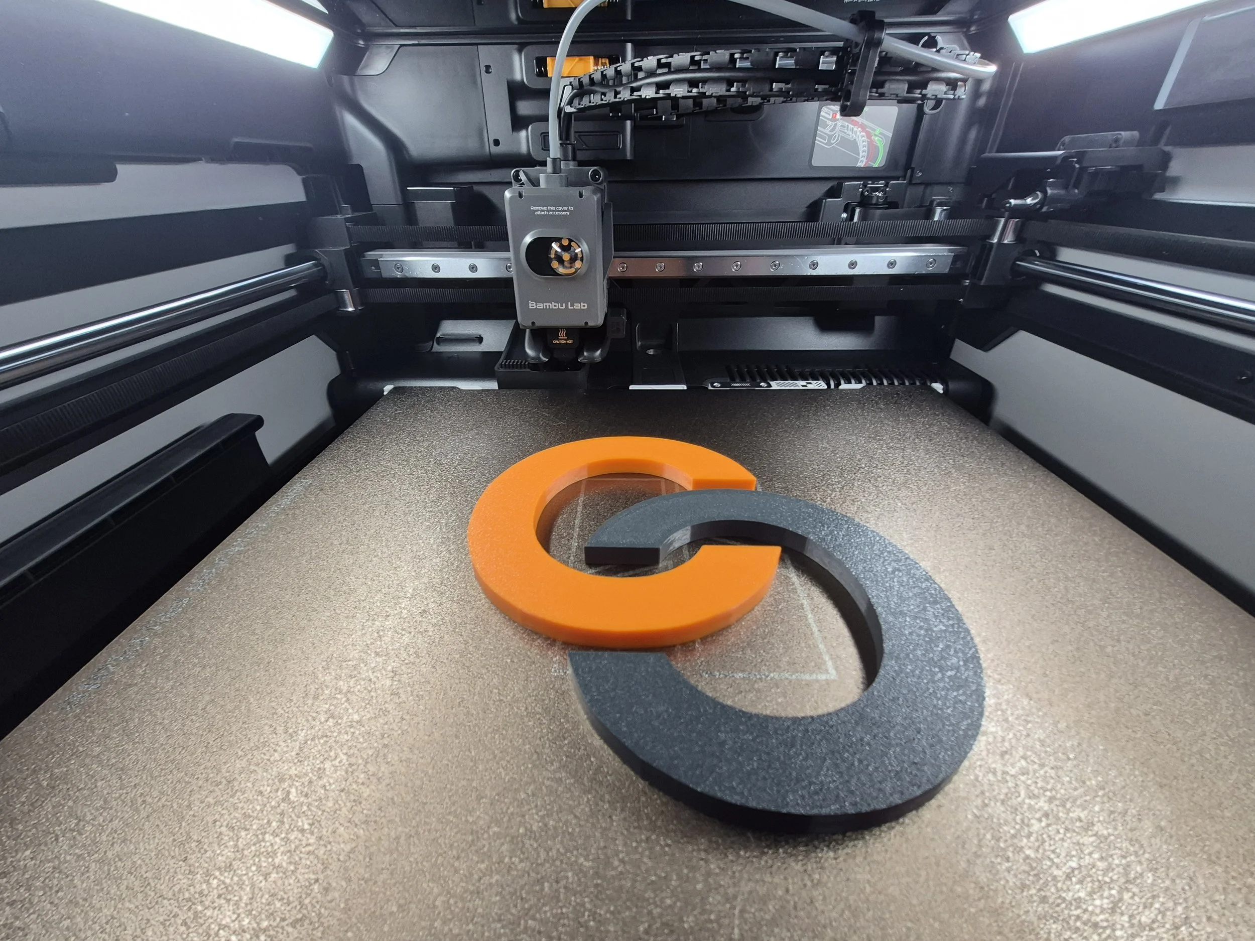 Vytištěný 3D díl v černo-oranžovém provedení na tiskové podložce 3D tiskárny.