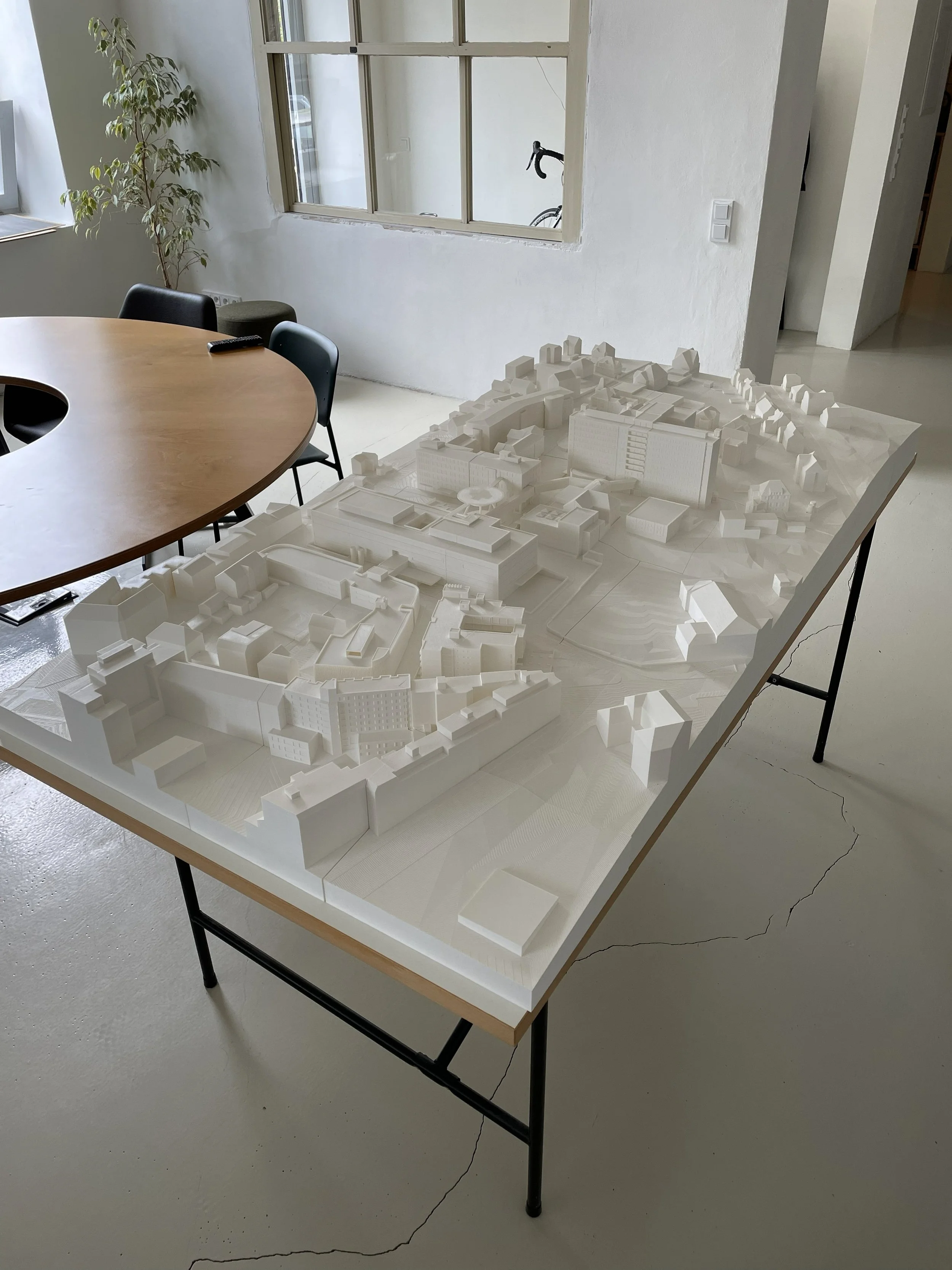 Bílý 3D tištěný architektonický model budovy umístěný na pracovním stole.