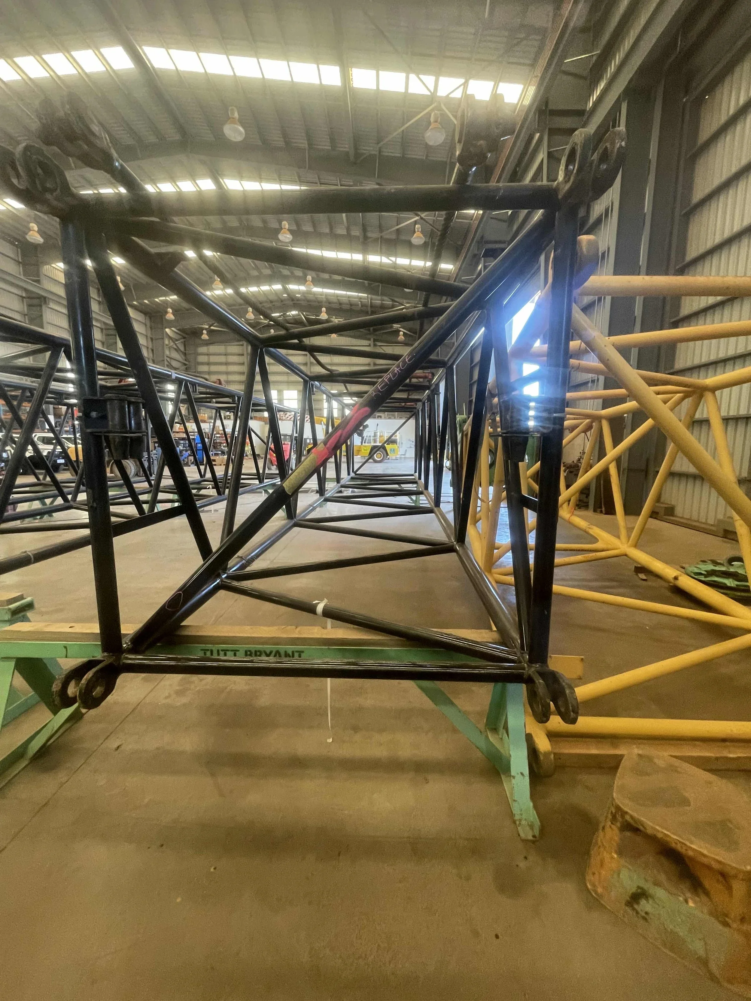Multiple colorful racing go-kart frames stacked in a warehouse with high ceiling and industrial lighting.