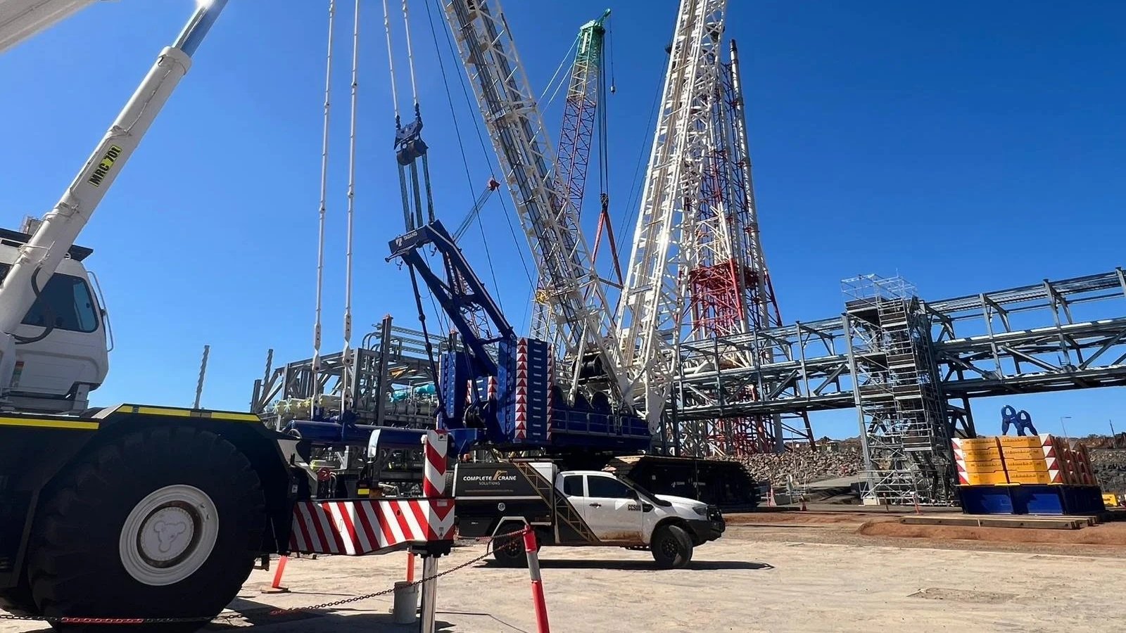 Construction site with large cranes, scaffolding, and construction vehicles under a clear blue sky.