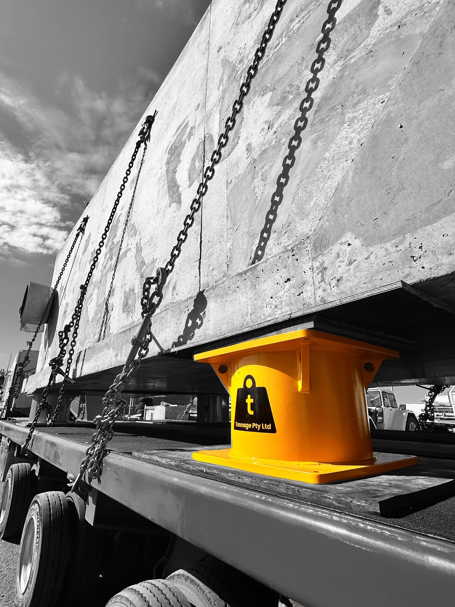 A close-up of chains hanging from a concrete wall and resting on a flatbed trailer, with a yellow support beam labeled 'tonnage Pty Ltd' underneath.