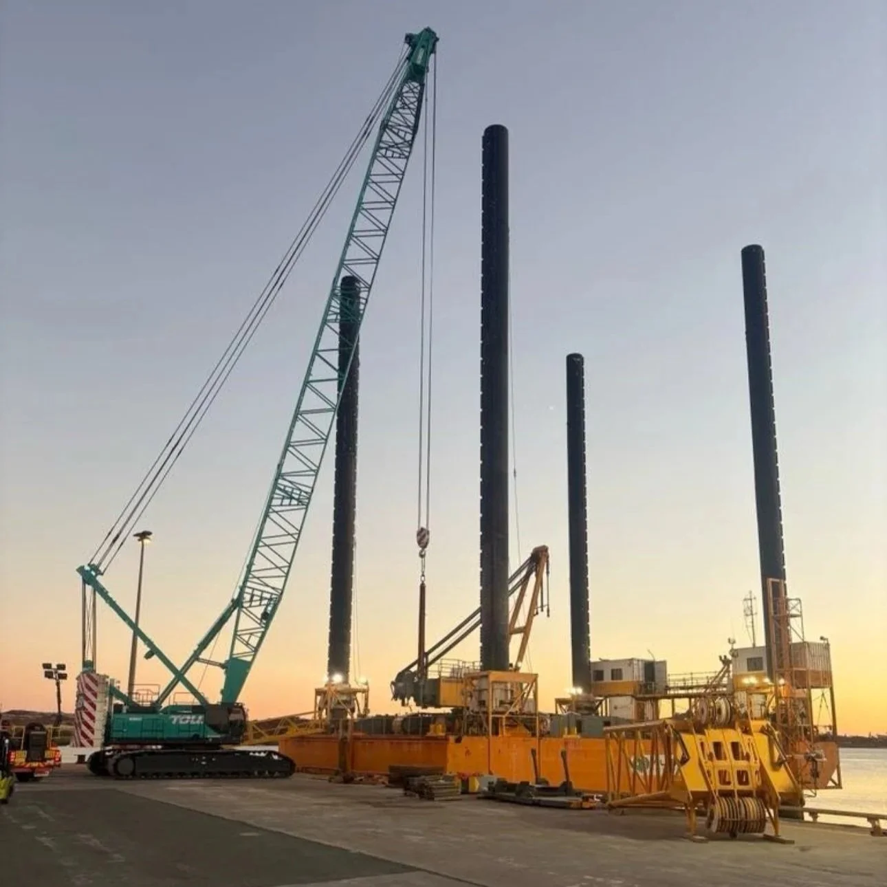 Construction site with cranes and drilling equipment at dusk.
