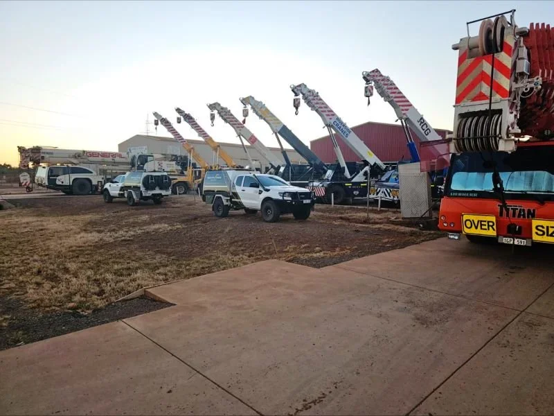 Multiple cranes and emergency vehicles parked on a dirt lot outside a red industrial building during sunset.