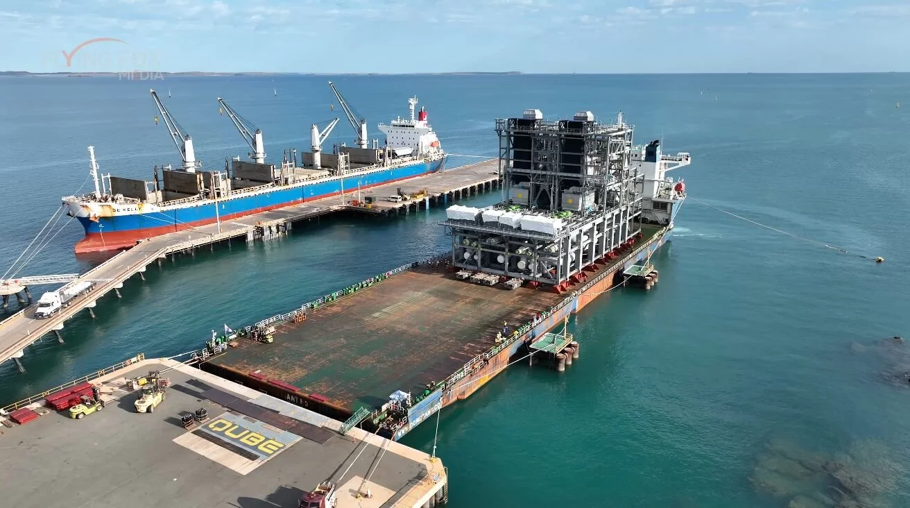 A large offshore oil production platform next to a supply ship in open water, with a clear blue sky.
