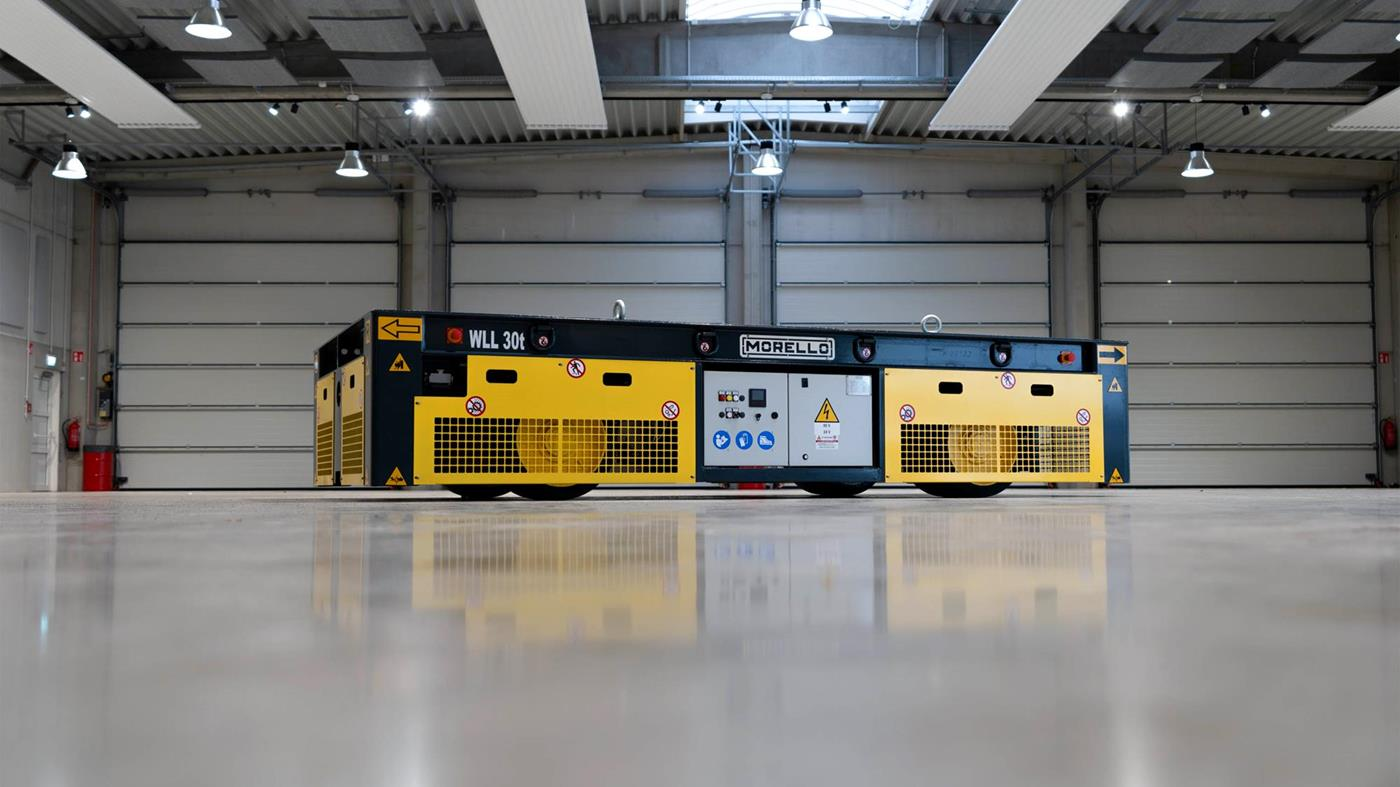 Yellow and black industrial robot inside a warehouse with a modern ceiling, closed roller doors, and overhead lighting.