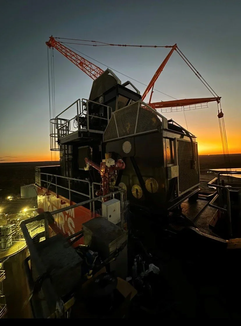 Industrial drilling rig at sunset with crane and equipment.
