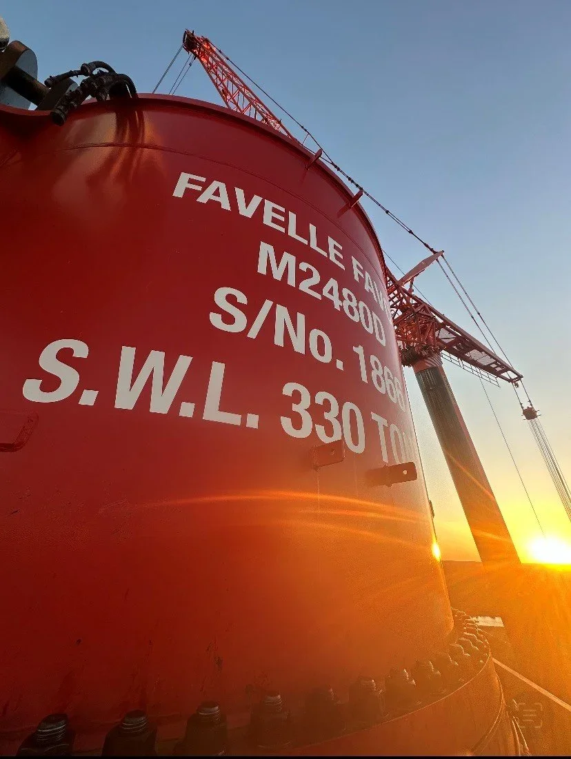 Close-up of a red industrial tank with white lettering displaying specifications, with a crane and a sunset in the background.