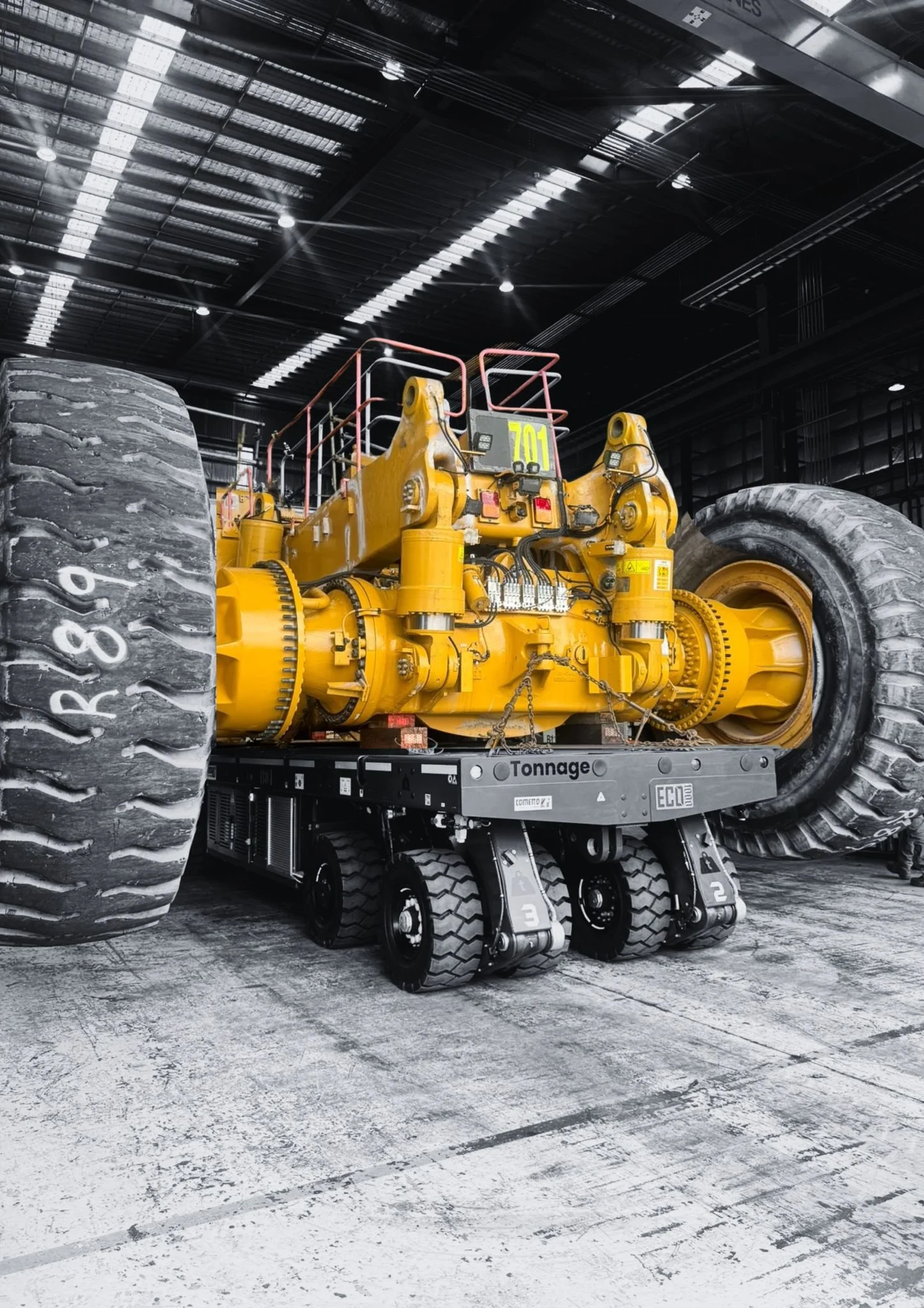 A large yellow industrial construction vehicle, possibly a bulldozer or front loader, inside a spacious industrial building or warehouse. The vehicle has oversized tires and is equipped with a large blade or scoop at the front.