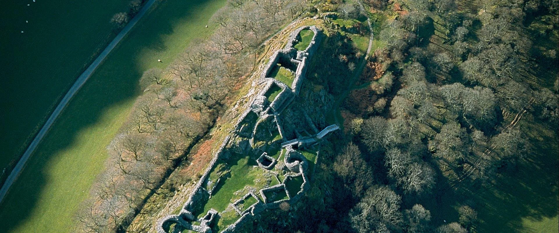 Aerial view looking down on Castell y Bere, Mid Wales. An ancient stone castle remains, build on rocky outcrop surrounded by green fields.