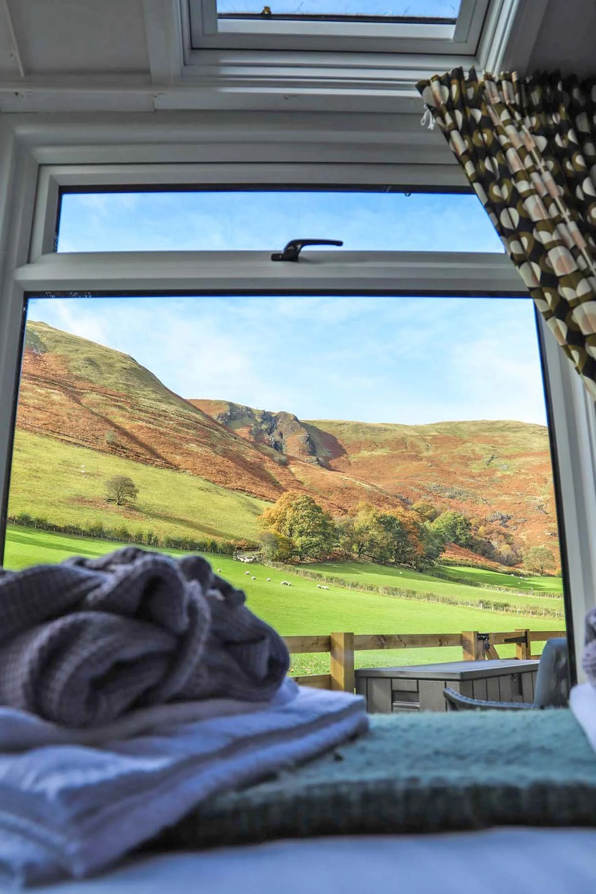 Window view of mountain ridge from within a holiday cabin. Bed sheets and blankets in foreground.
