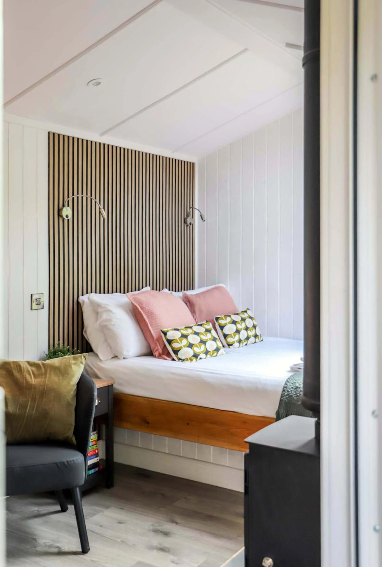 timber holiday cabin bedroom space with grey upholstered armchair, textured vertical timber wall cladding