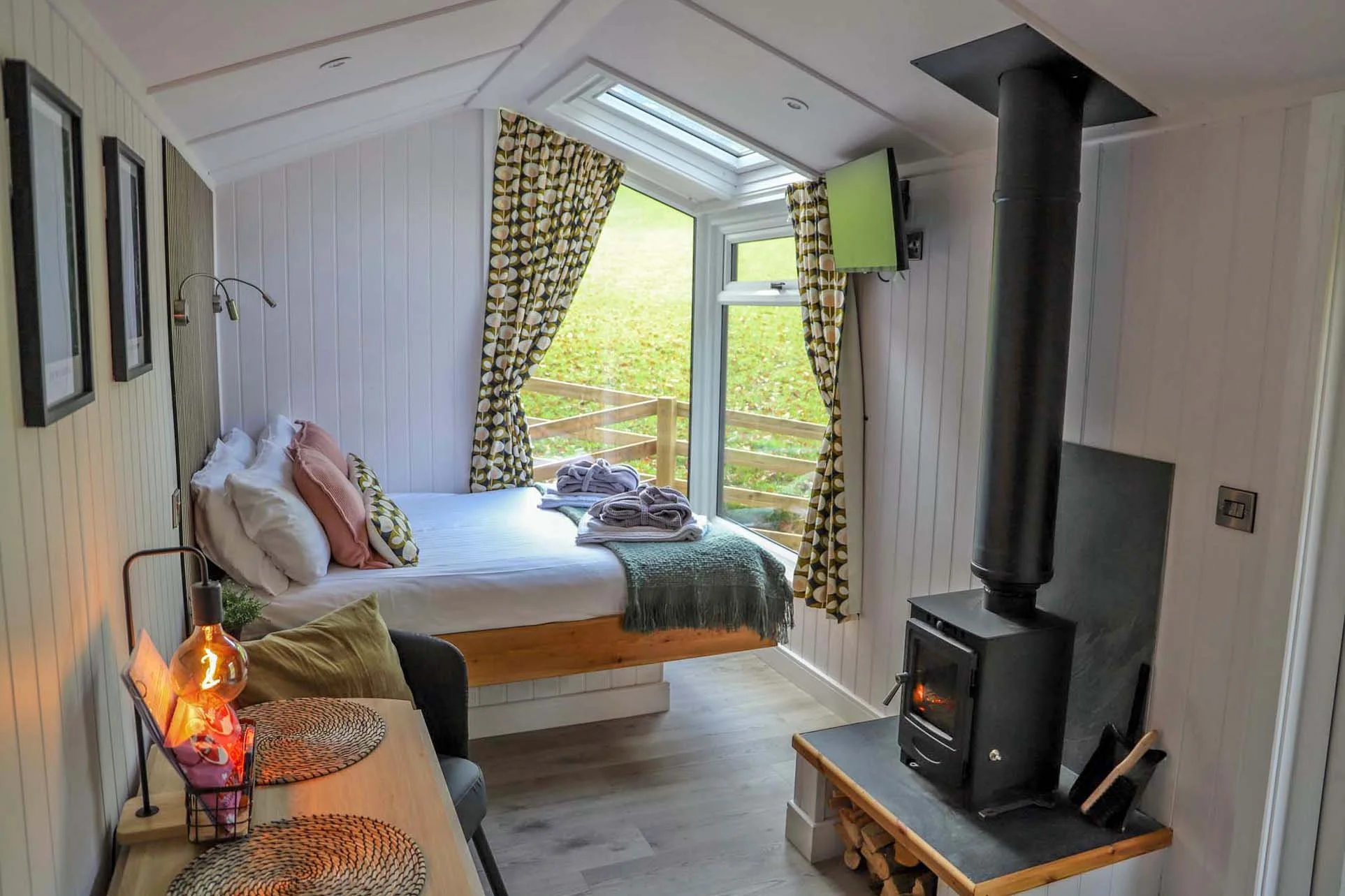 modern holiday timber cabin interior with light painted walls, floating double bed and wood-burning stove.