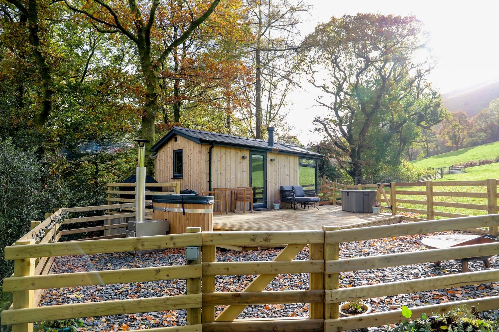 Modern timber holiday cabin and decking area within a fenced enclosure, set within mature oak trees in autumnal colours, set in the hills Mid Wales Eryri National Park