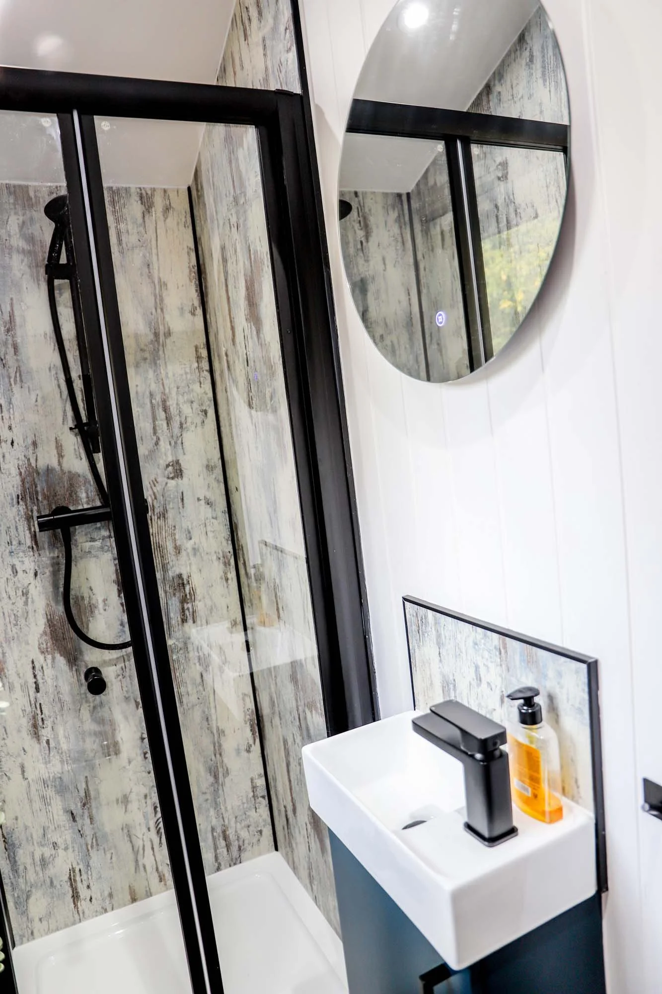 compact holiday cabin bathroom with shower and small modern basin. Shower has dark framed enclosure and aged timber effect wall panels.