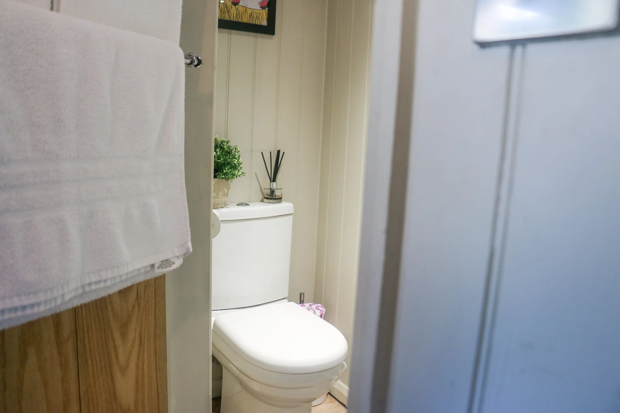 View of a small bathroom toilet with towel and decorative items, partially viewed through a door.