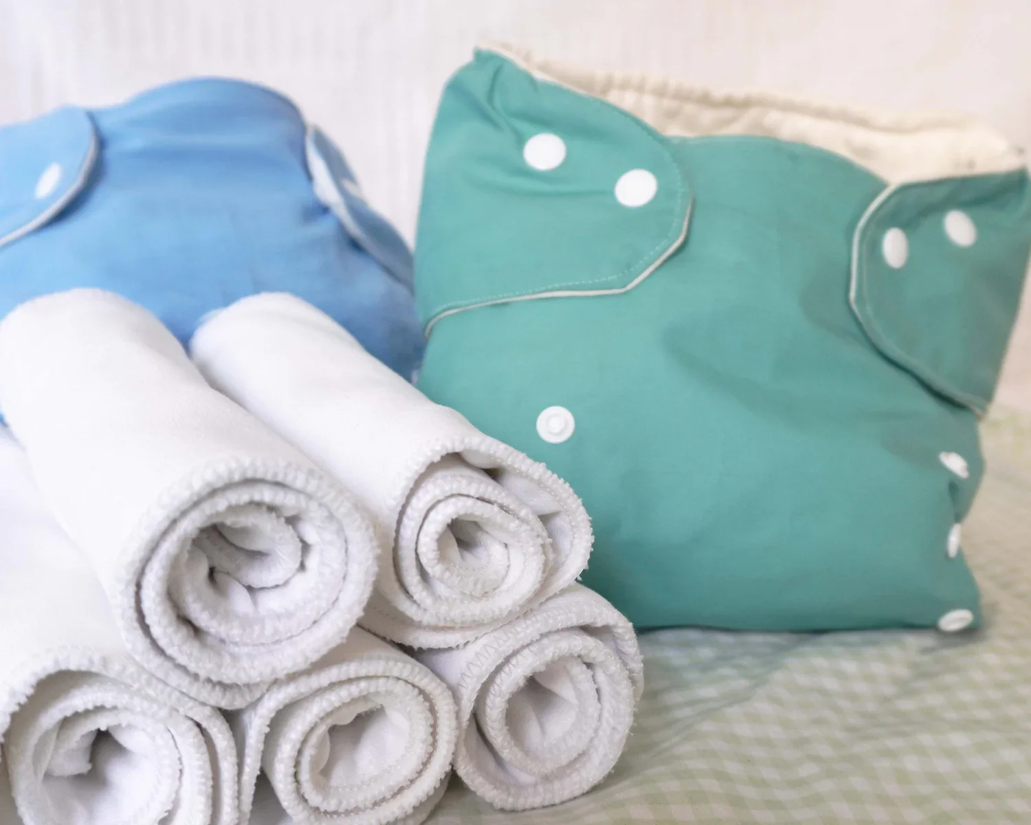 A pile of reusable diapers on a bed, some white, some blue and green.